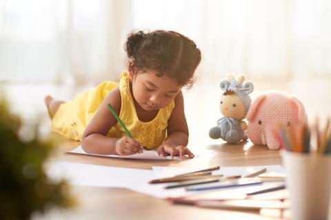 Young child lying on the floor and coloring page with crayons